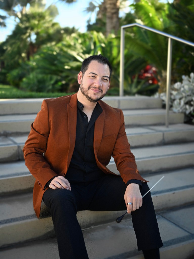 Martín Alexander Arellano seated outdoors holding a conductor’s baton