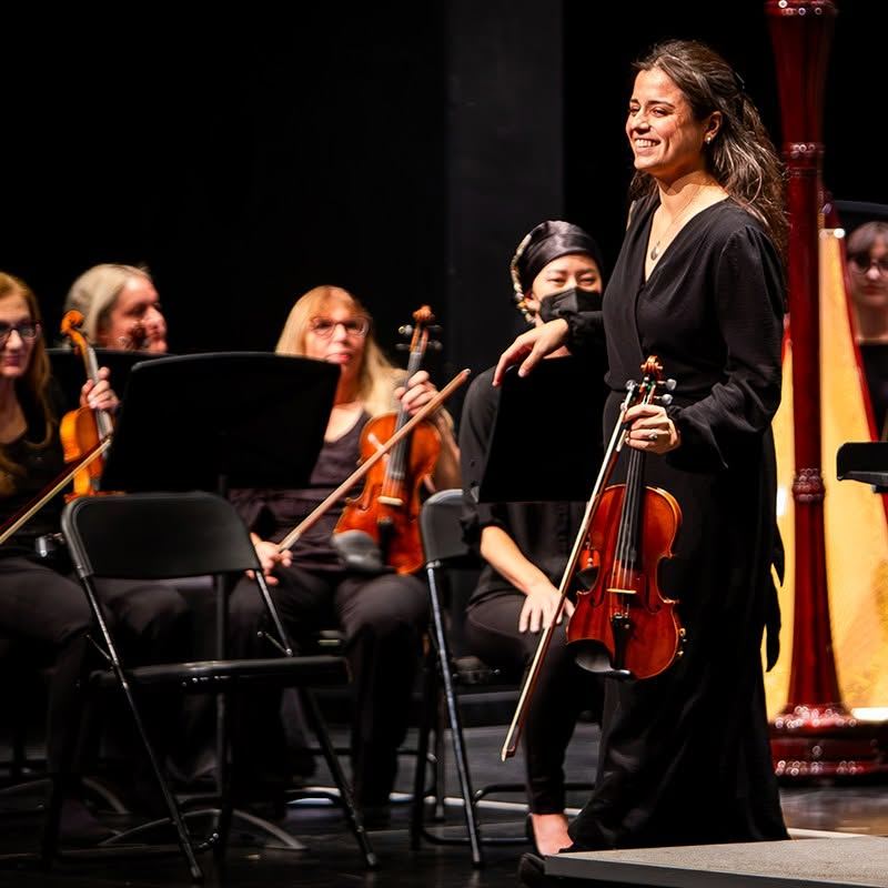 A smiling violinist takes a bow with the orchestra